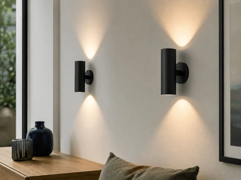 Modern black wall sconces on a white wall with a window and decor items in the background.